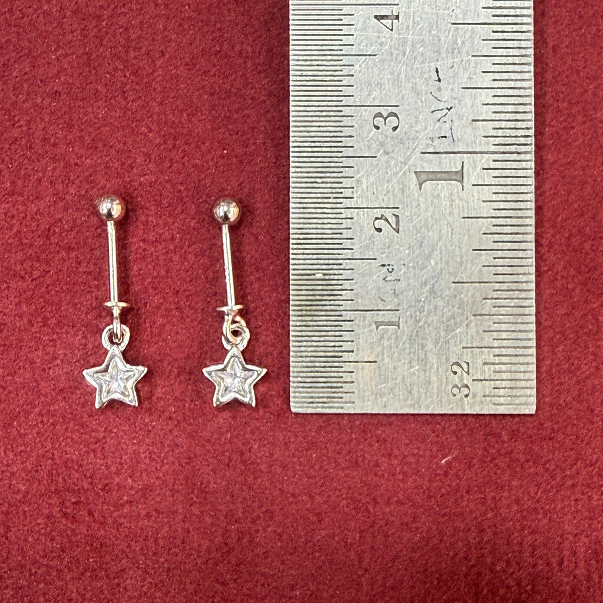 Silver star-shaped earrings on a red surface with a ruler for scale.