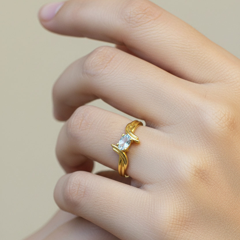 Gold ring with a diamond on a person's finger against a red fabric background