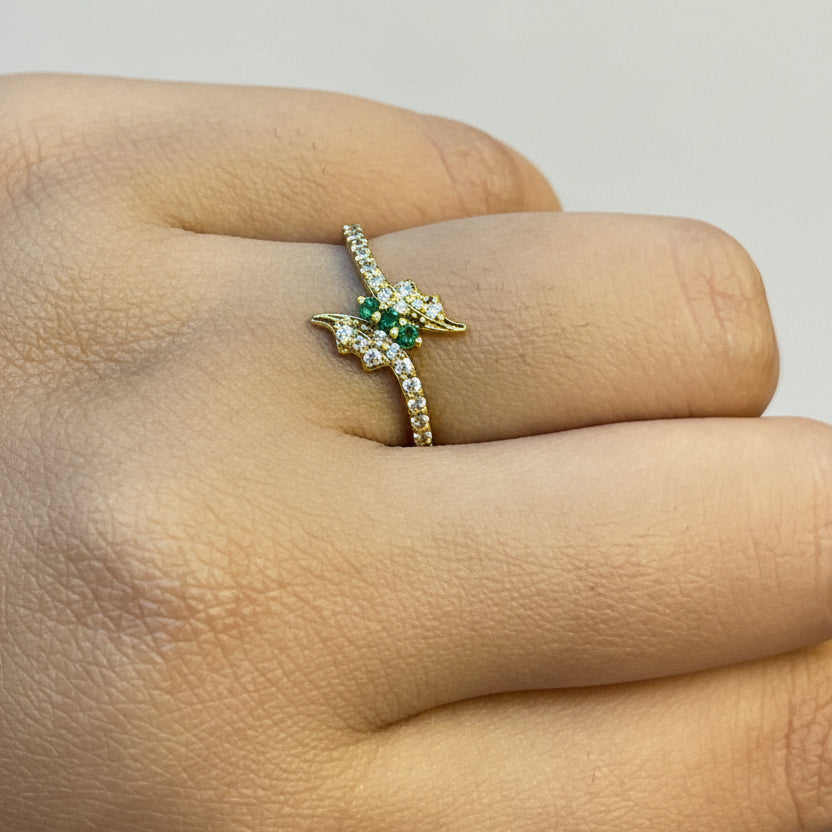 Gold ring with green gemstone on a finger against a red fabric background