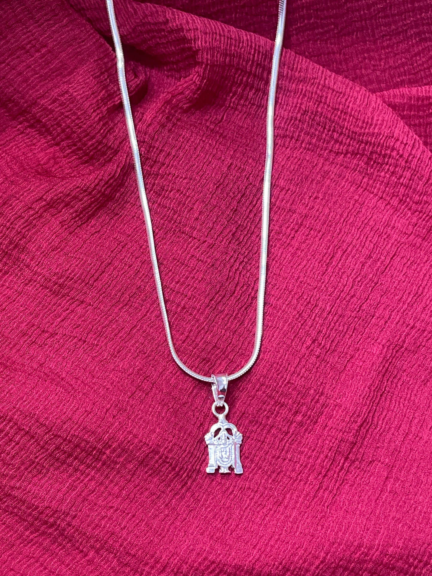 Silver necklace with a small pendant on a red fabric background