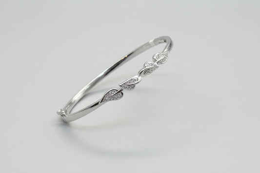 Silver bracelet with leaf designs held in a hand against a red fabric background