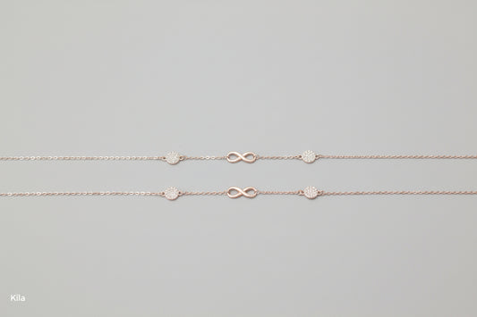 Two silver necklaces with infinity symbols on a teal fabric background