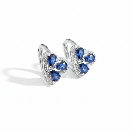 Two rings with blue gemstones on a hand against a pink background