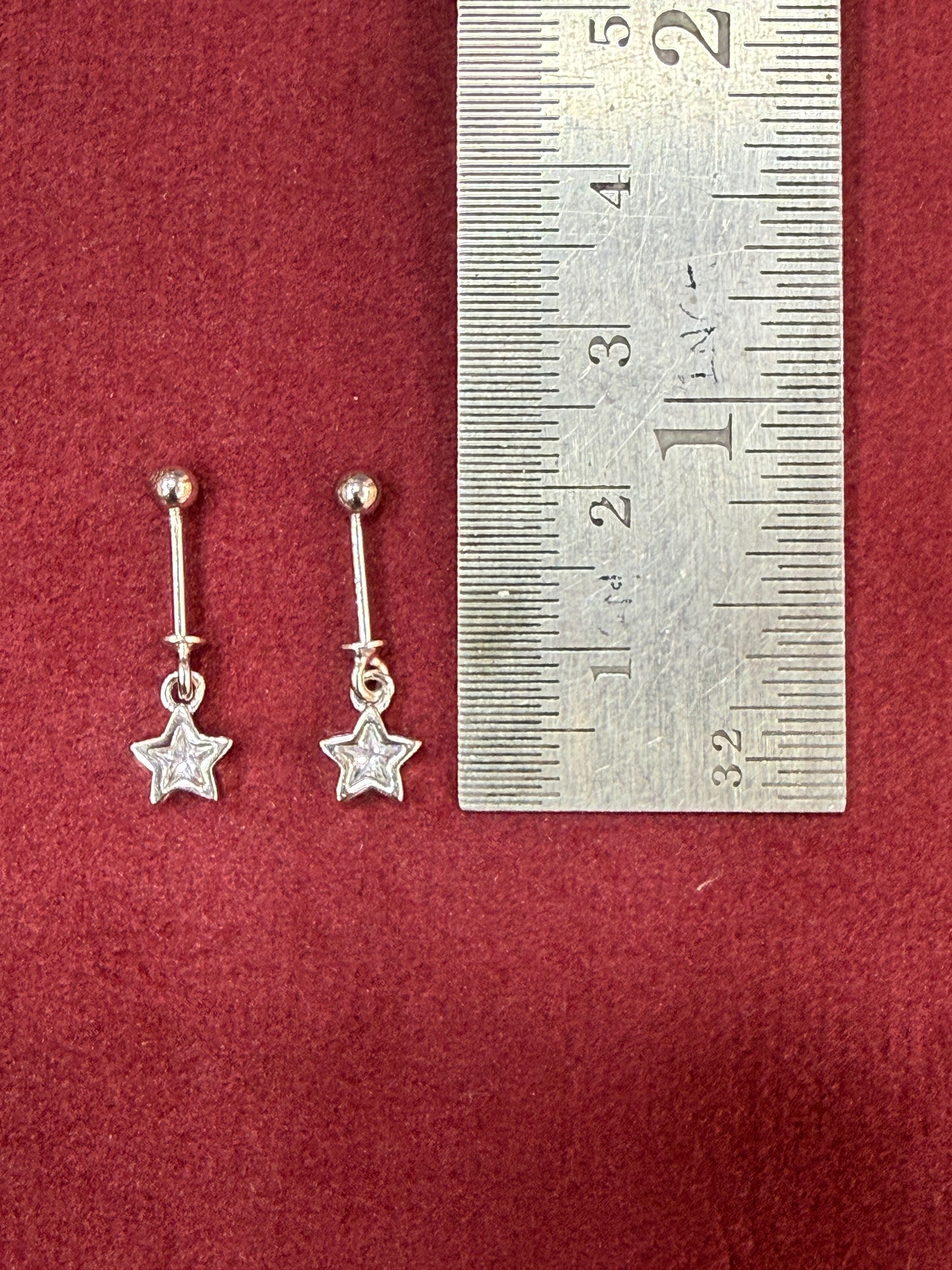 Silver star-shaped earrings on a red surface with a ruler for scale.