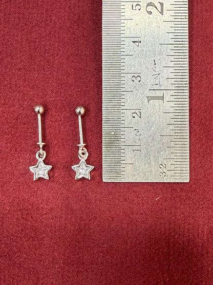 Silver star-shaped earrings on a red surface with a ruler for scale.