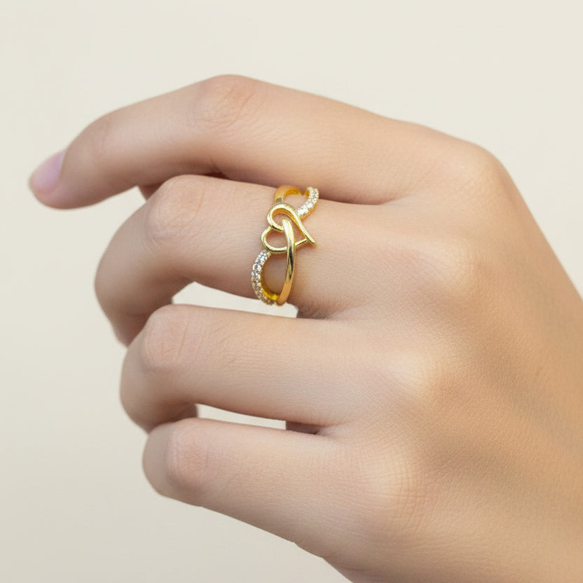 Gold ring with heart design on a finger against a red fabric background