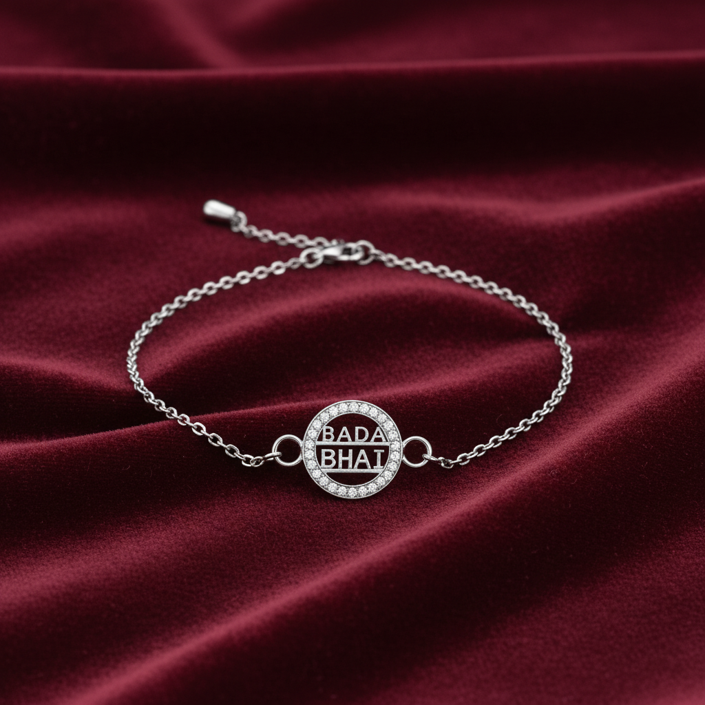 A silver chain bracelet with a circular pavé centerpiece engraved with 'BADA BHAi' in black lettering, displayed on a draped dark red velvet fabric.