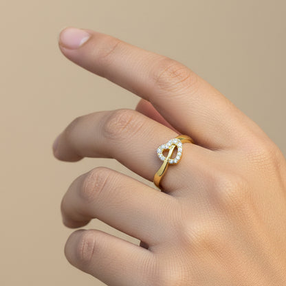 Gold ring with heart design on a finger against a red fabric background