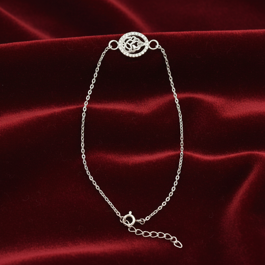 A delicate silver chain bracelet with a circular pavé-style clasp and an adjustable lobster clasp extension, displayed on a draped dark red velvet fabric background.