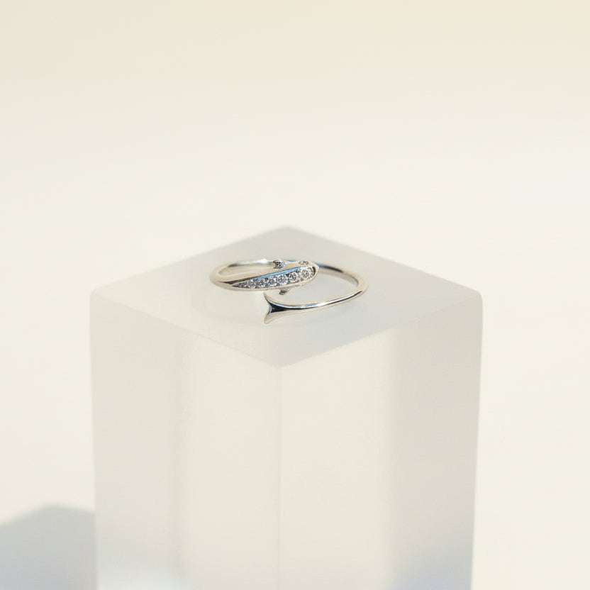 Silver ring with a diamond on a white pedestal against a light beige background