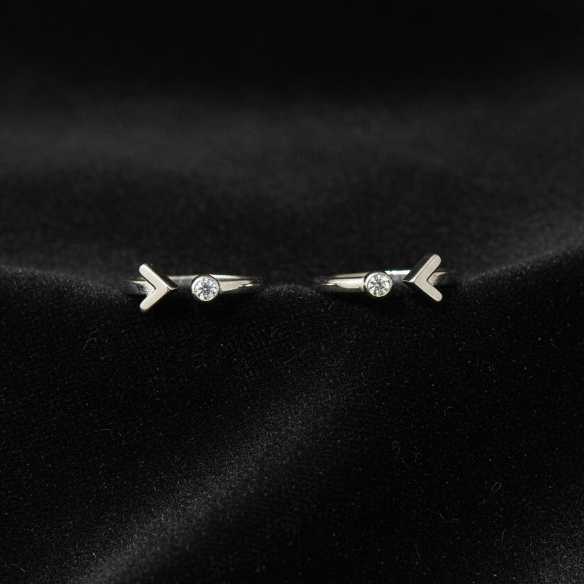 Two silver rings with arrow designs on a pink fabric background.