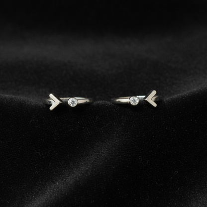 Two silver rings with arrow designs on a pink fabric background.