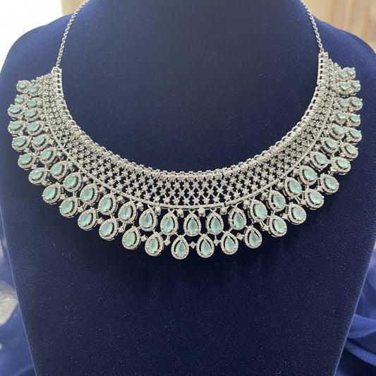 Silver necklace with green gemstones on a red velvet cushion