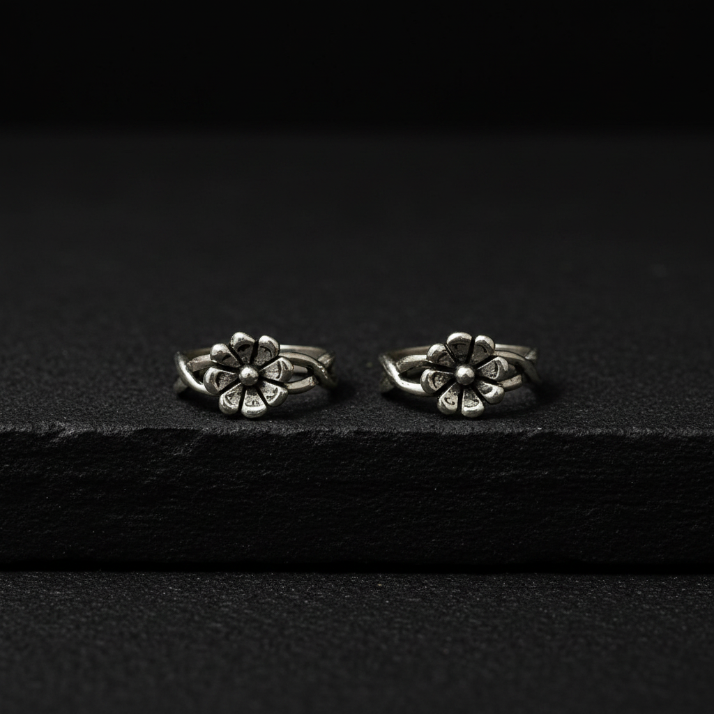 Two silver flower-shaped earrings on a pink fabric background