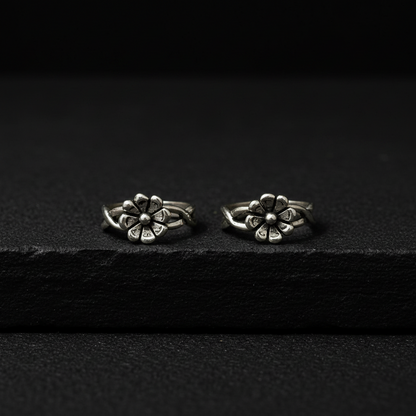 Two silver flower-shaped earrings on a pink fabric background