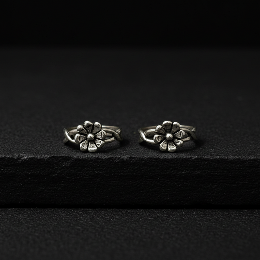 Two silver flower-shaped earrings on a pink fabric background