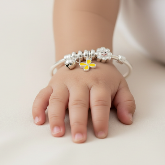 Child's hand wearing a bracelet with a yellow flower charm on a light background