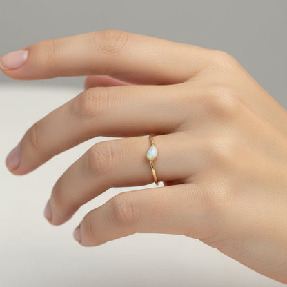 Gold ring with a small stone on a finger against a red fabric background