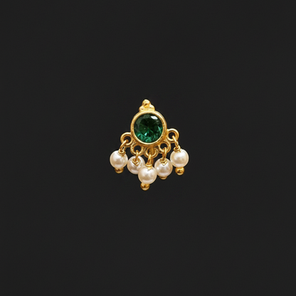 Gold ring with green gemstone and pearls on a finger against a red fabric background
