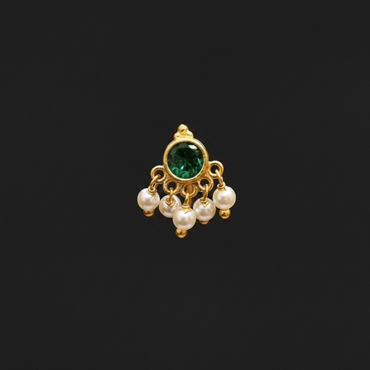 Gold ring with green gemstone and pearls on a finger against a red fabric background
