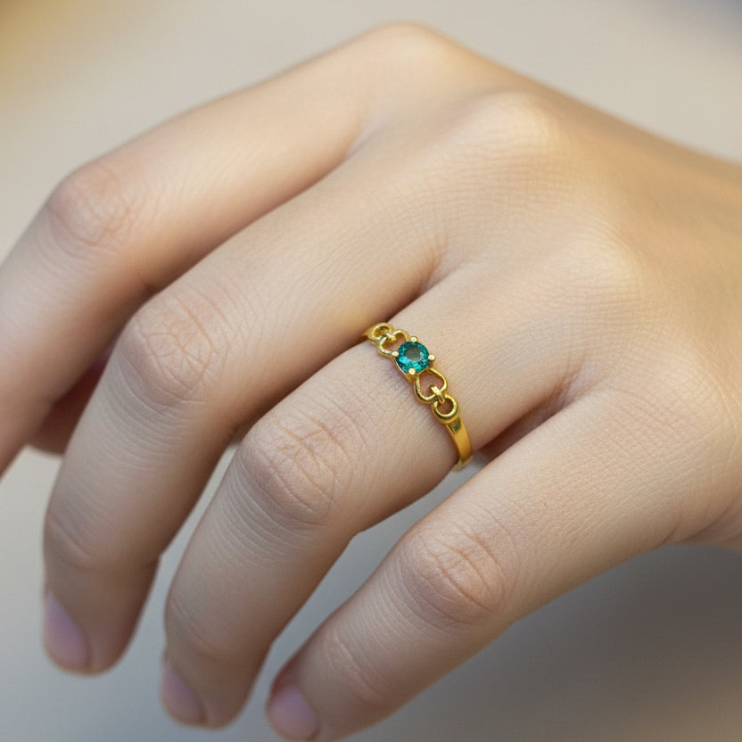Gold ring with a green gemstone on a finger against a red fabric background