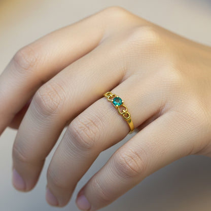 Gold ring with a green gemstone on a finger against a red fabric background
