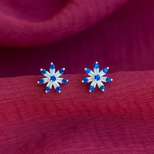 Snowflake-shaped earrings with blue gemstones on a finger against a red fabric background