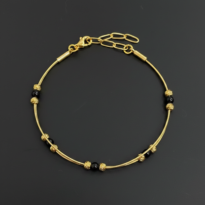 Gold bracelet with black beads on a red textured fabric background