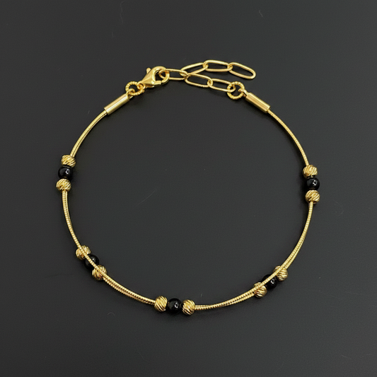 Gold bracelet with black beads on a red textured fabric background