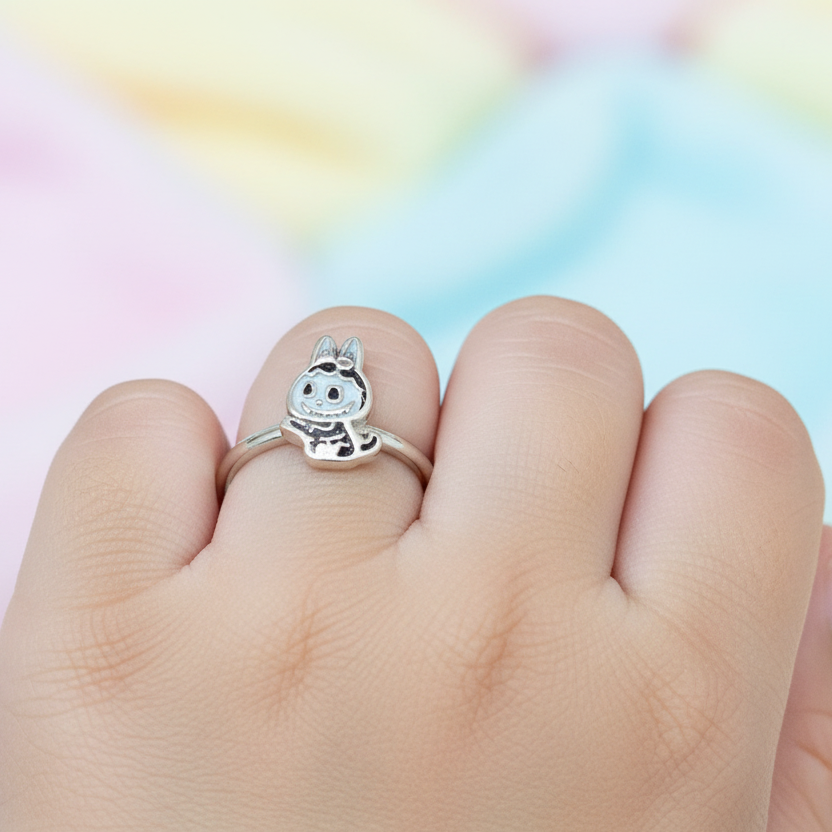 Hand wearing a silver ring with a cartoon character on a colorful background