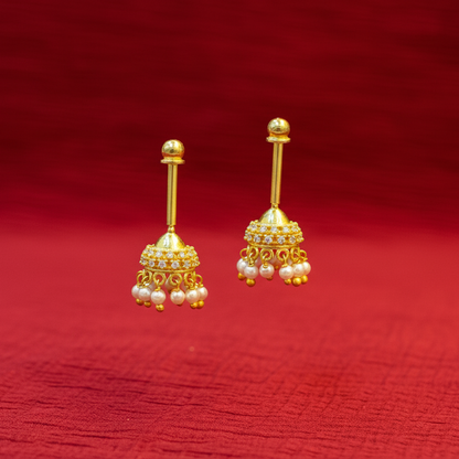 Gold earrings with pearl drops on a red fabric background