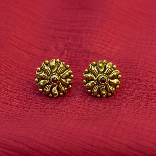 Gold floral earrings on a person's fingers against a red background
