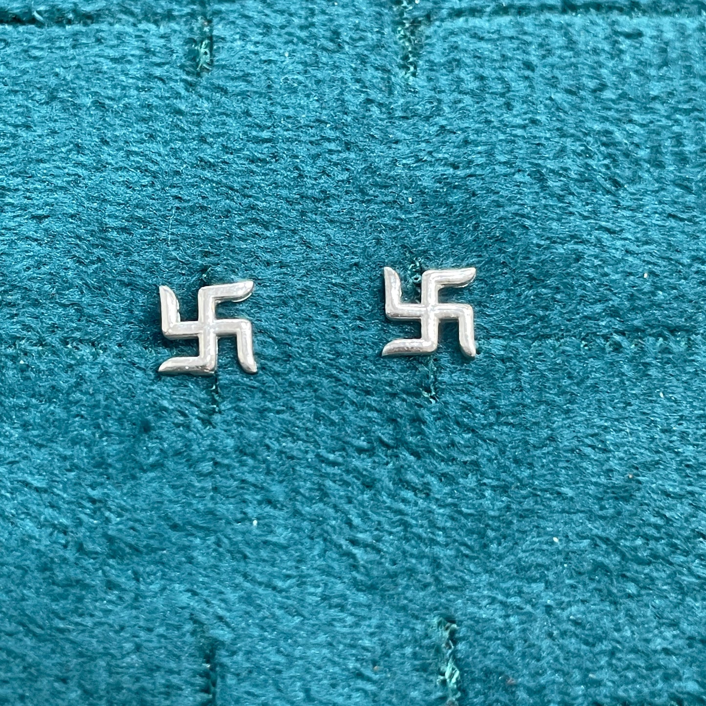 Two silver swastika symbols on a textured blue fabric background