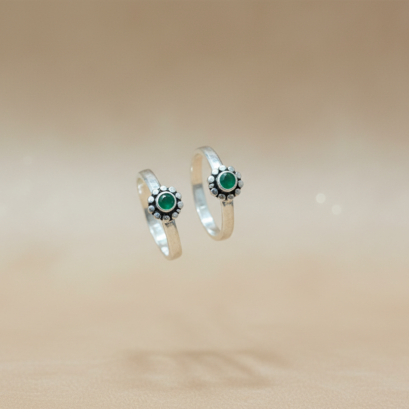 Two silver rings with green gemstones on a beige background