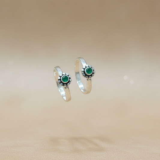 Two silver rings with green gemstones on a beige background