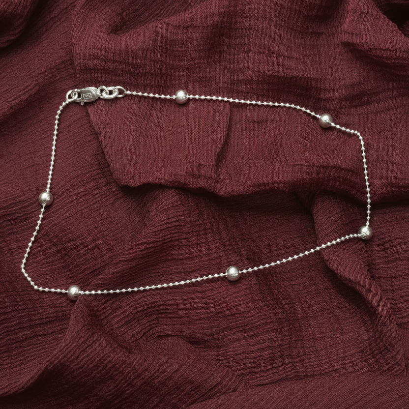 Silver beaded necklace on a red textured fabric background