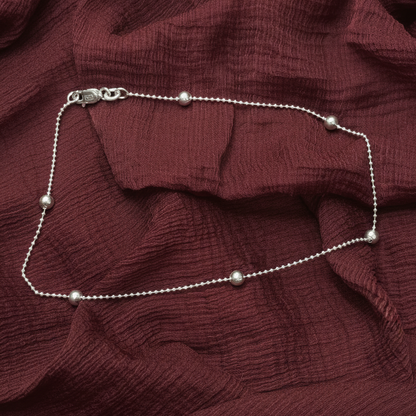 Silver beaded necklace on a red textured fabric background