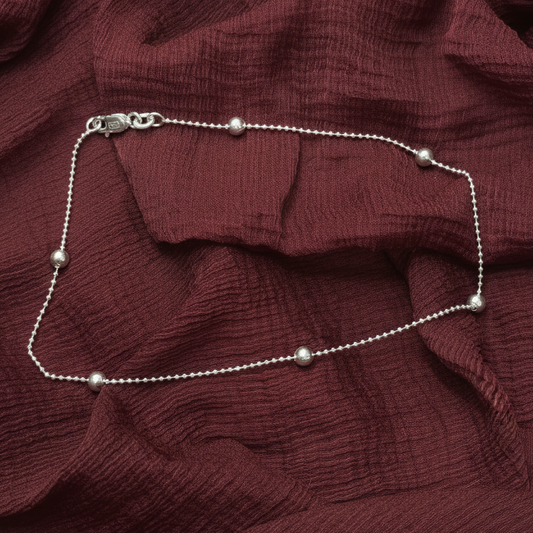 Silver beaded necklace on a red textured fabric background