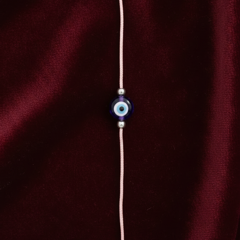 Bracelet with a blue evil eye charm on a maroon fabric background