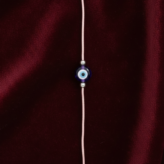 Bracelet with a blue evil eye charm on a maroon fabric background