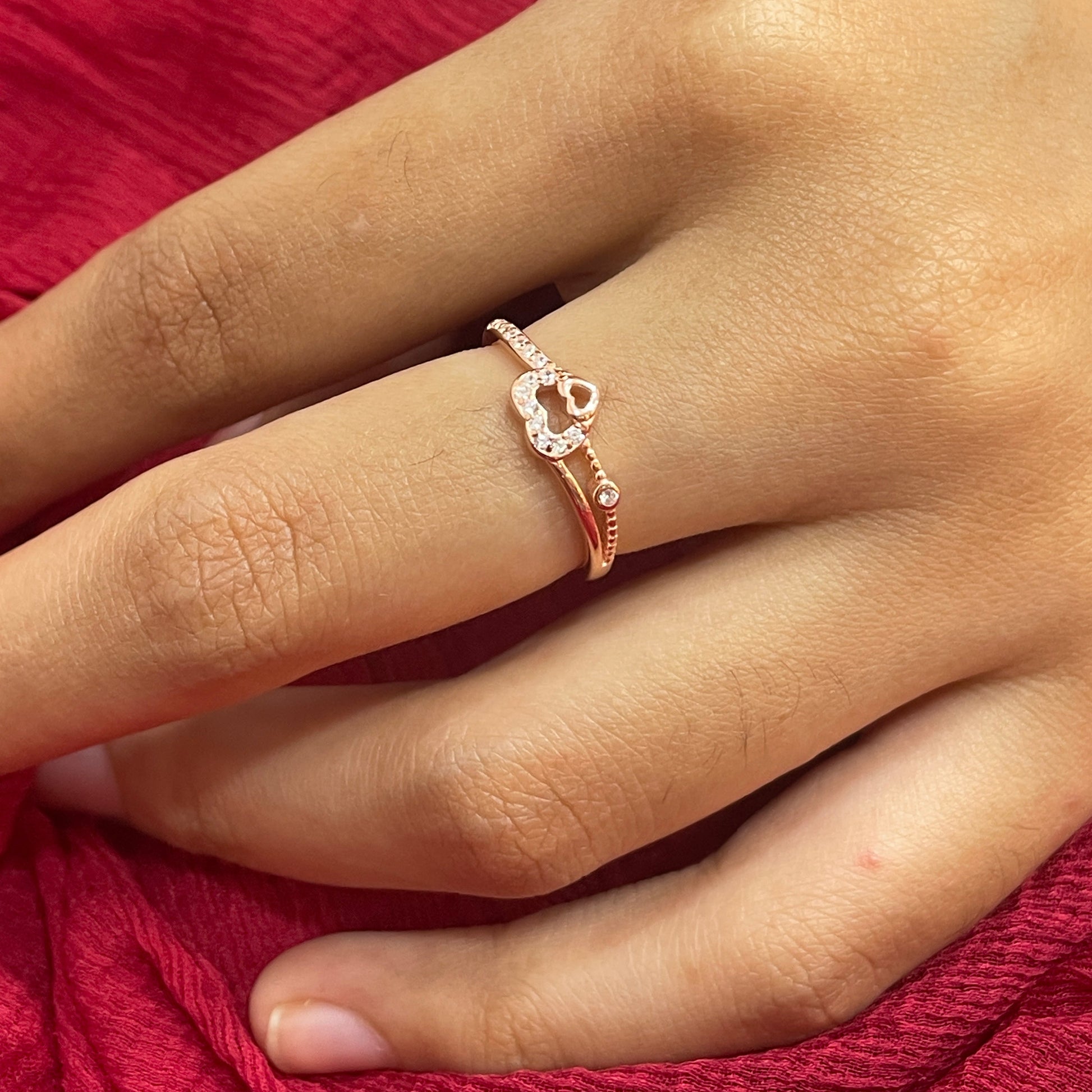 Hand wearing a rose gold ring with a red fabric background