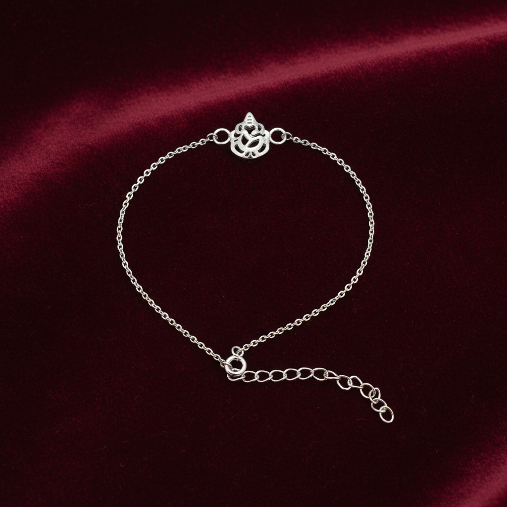 A delicate silver chain bracelet with a decorative ganesh symbol clasp and an adjustable extender chain, displayed on a dark red satin fabric background.