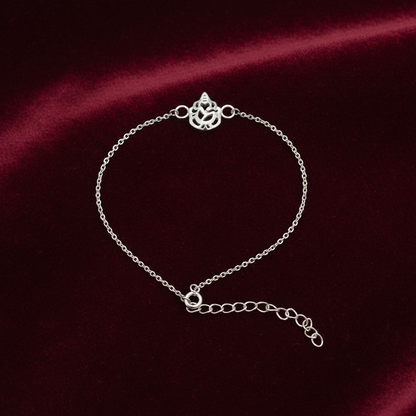 A delicate silver chain bracelet with a decorative ganesh symbol clasp and an adjustable extender chain, displayed on a dark red satin fabric background.
