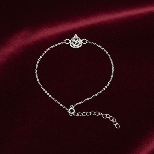 A delicate silver chain bracelet with a decorative ganesh symbol clasp and an adjustable extender chain, displayed on a dark red satin fabric background.