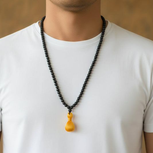 Person wearing a white t-shirt with a black beaded necklace featuring a yellow pendant.