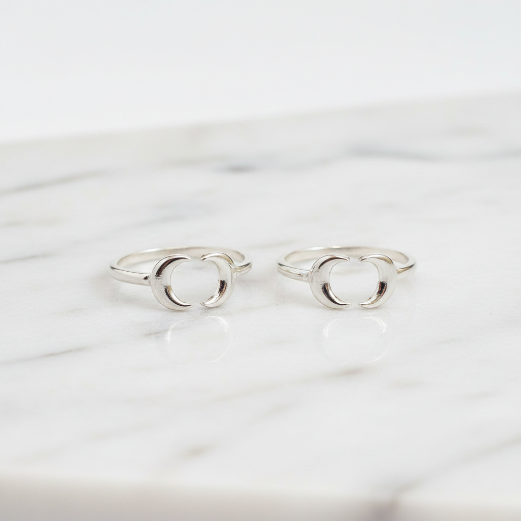 Two silver toe rings with a minimalist open interlocking circular design, displayed on a white marble surface.