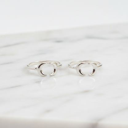 Two silver toe rings with a minimalist open interlocking circular design, displayed on a white marble surface.