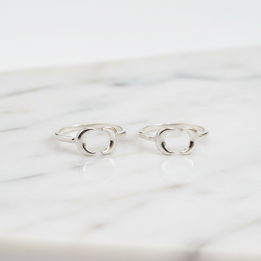 Two silver toe rings with a minimalist open interlocking circular design, displayed on a white marble surface.