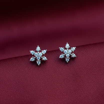 Silver snowflake earrings on a person's hand with a red fabric background