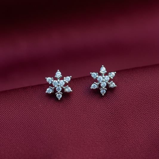 Silver snowflake earrings on a person's hand with a red fabric background